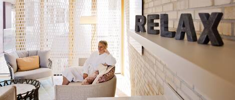 A spa-like setting with a person relaxing on a chair, a wicker sofa, and a wall with the word "RELAX" in large letters.