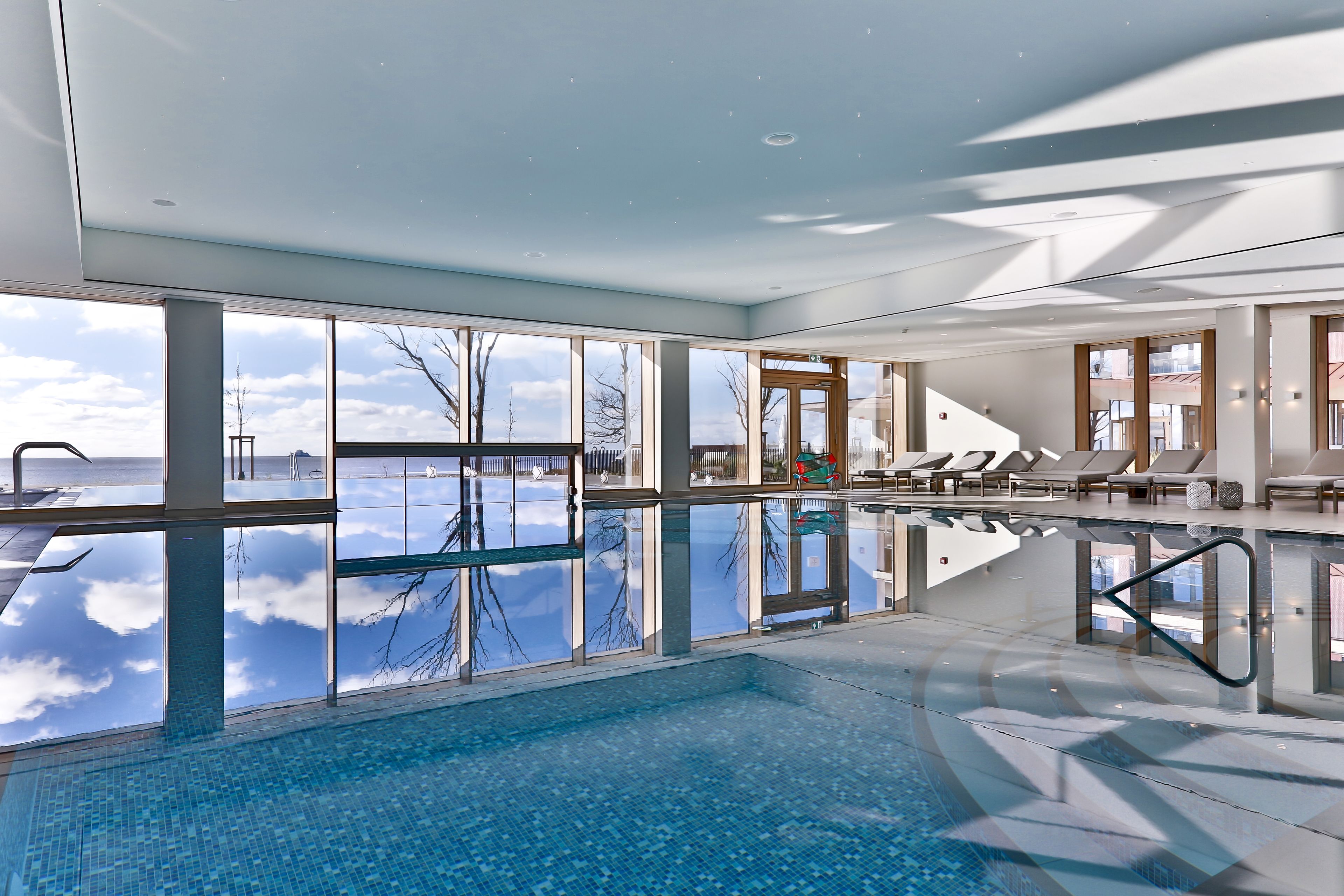 Una piscina interior moderna con grandes ventanales que ofrecen vistas al cielo y las nubes.