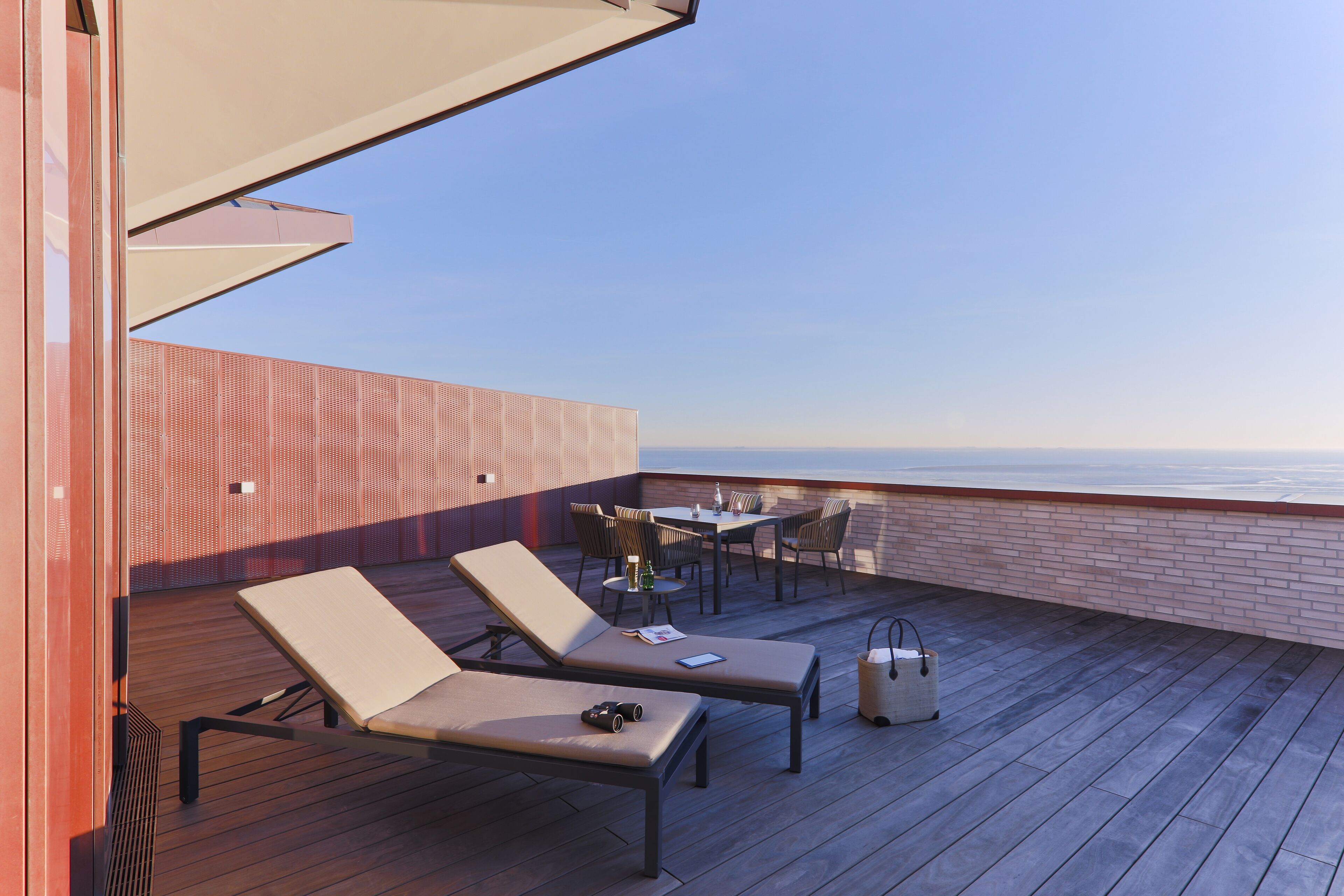 A rooftop terrace with two lounge chairs, a table, and chairs, overlooking a body of water.