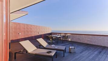 A rooftop terrace with two lounge chairs, a table, and chairs, overlooking a body of water.