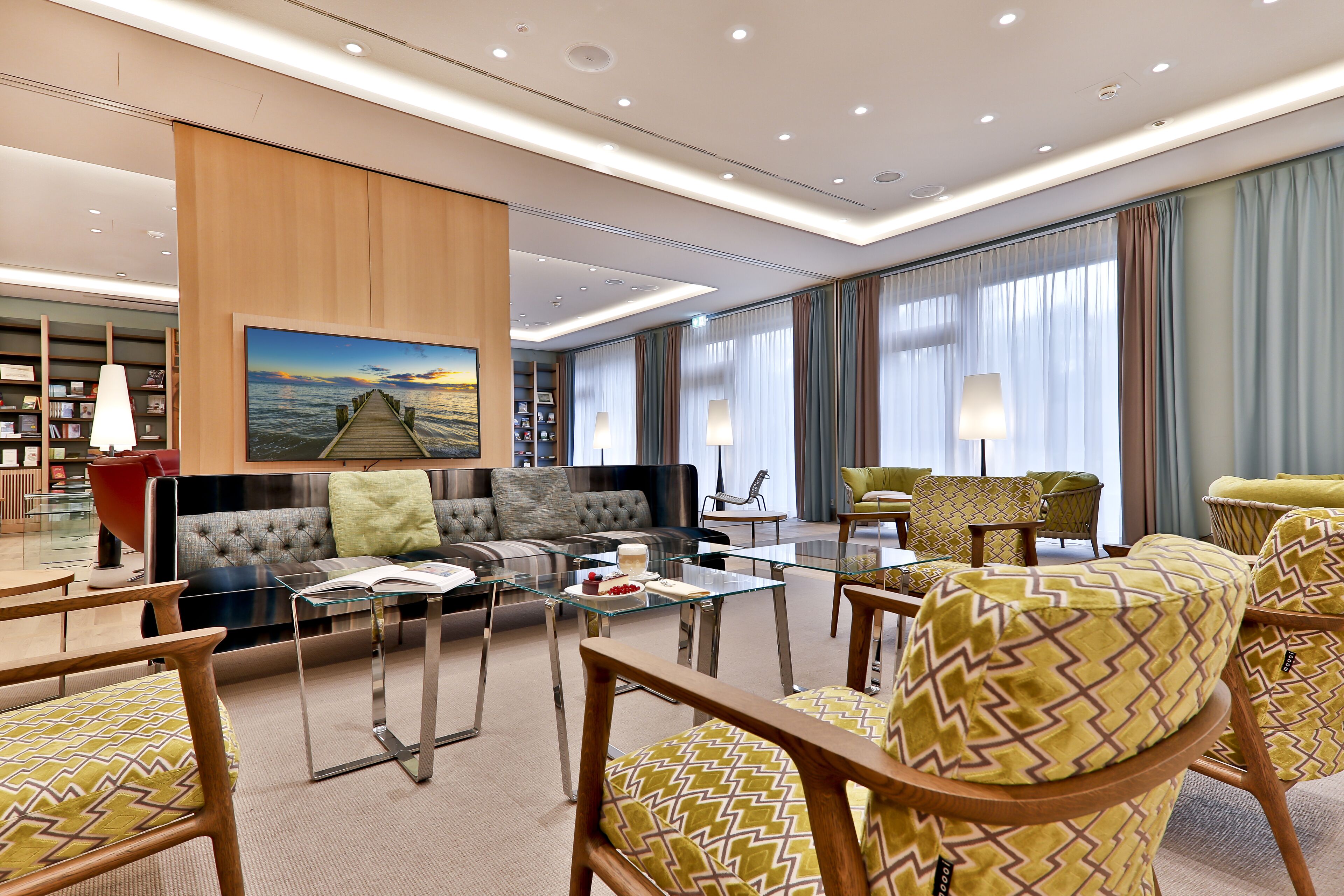 A modern hotel lobby with a seating area, a glass coffee table, and a bookshelf.