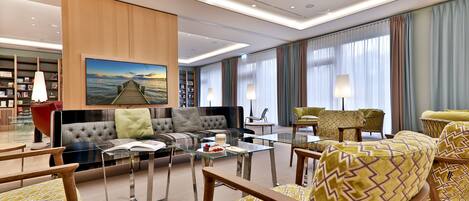 A modern hotel lobby with a seating area, a glass coffee table, and a bookshelf.