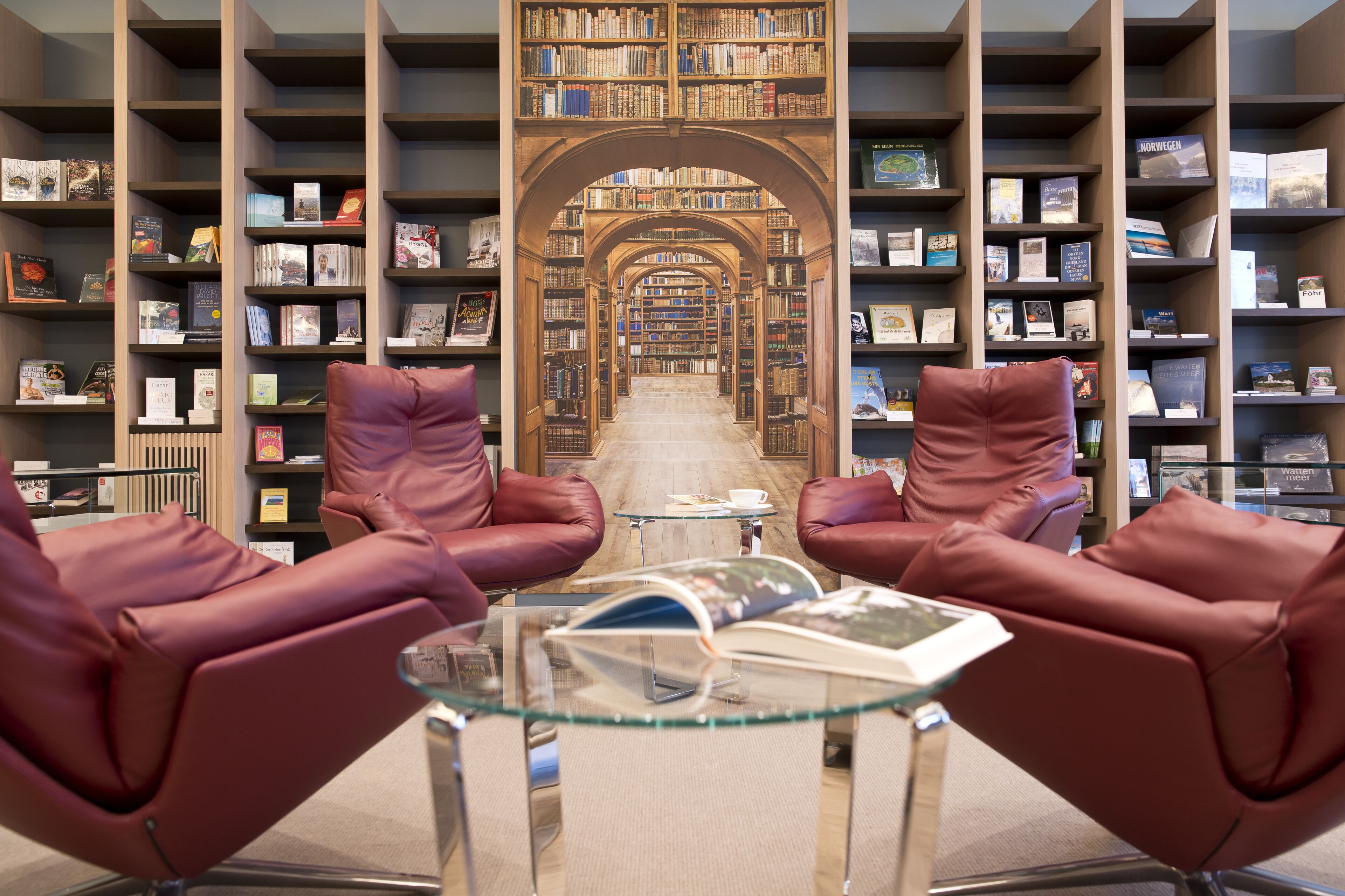 A library with leather chairs, a glass table, and bookshelves filled with books.