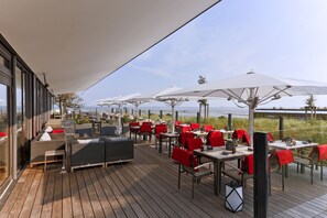 Un área de comedor al aire libre con mesas, sillas, sombrillas y vista al mar.