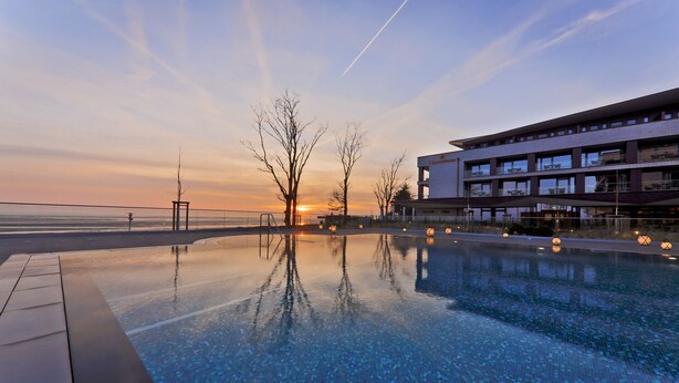 A modern hotel with a pool reflecting the sunset, a clear sky, and a view of the sea. - Upstalsboom Wyk auf Föhr (Wyk auf Foehr)