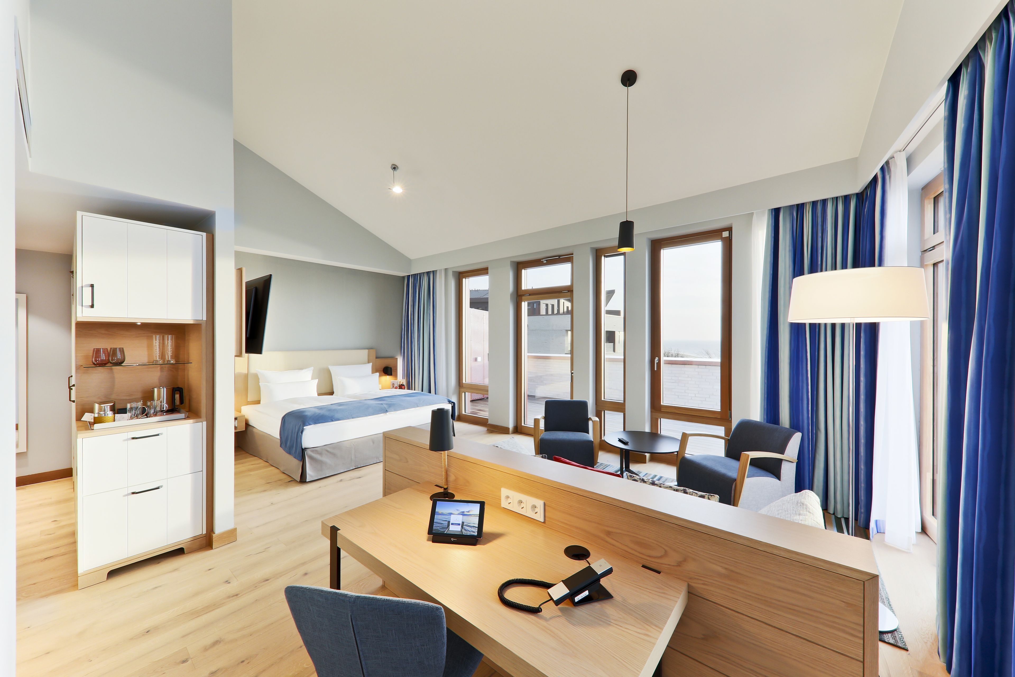 A modern hotel room with a bed, desk, chair, and a small table.