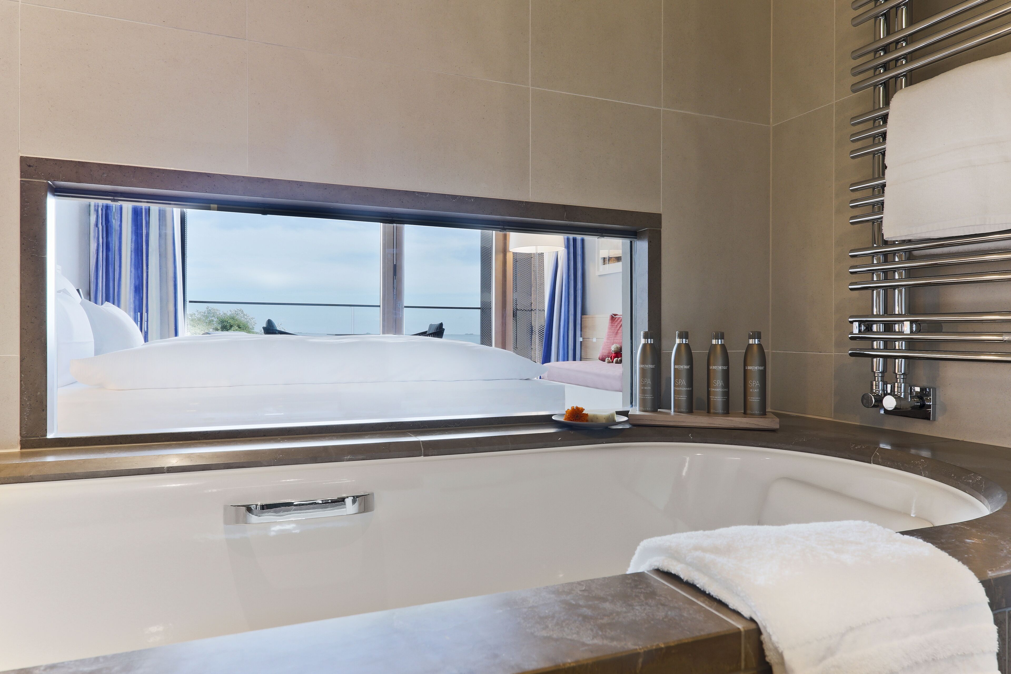 A modern bathroom with a large bathtub, a window with curtains, and a towel rack.