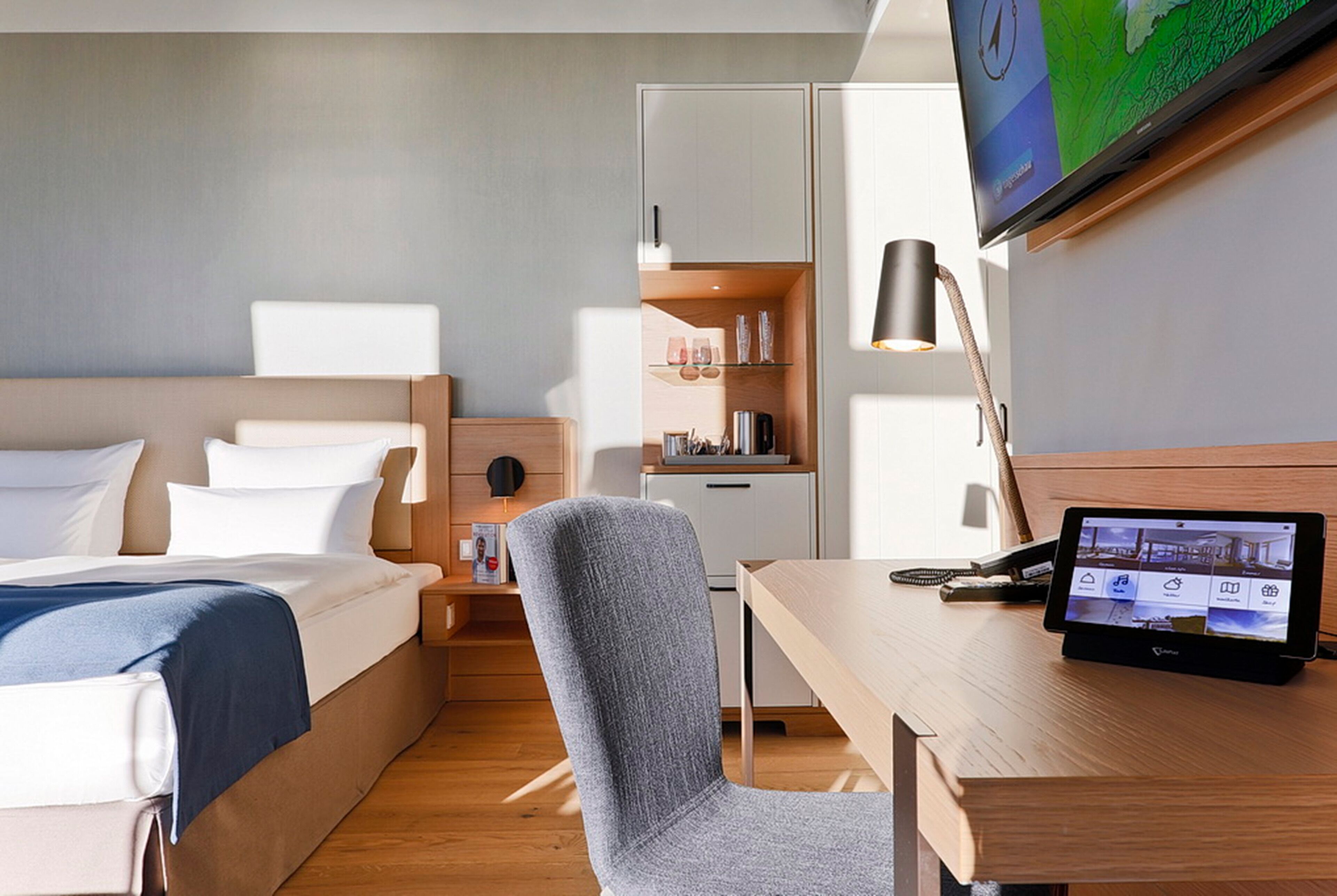 A hotel room with a bed, a desk with a computer, a chair, a TV, and a wardrobe.