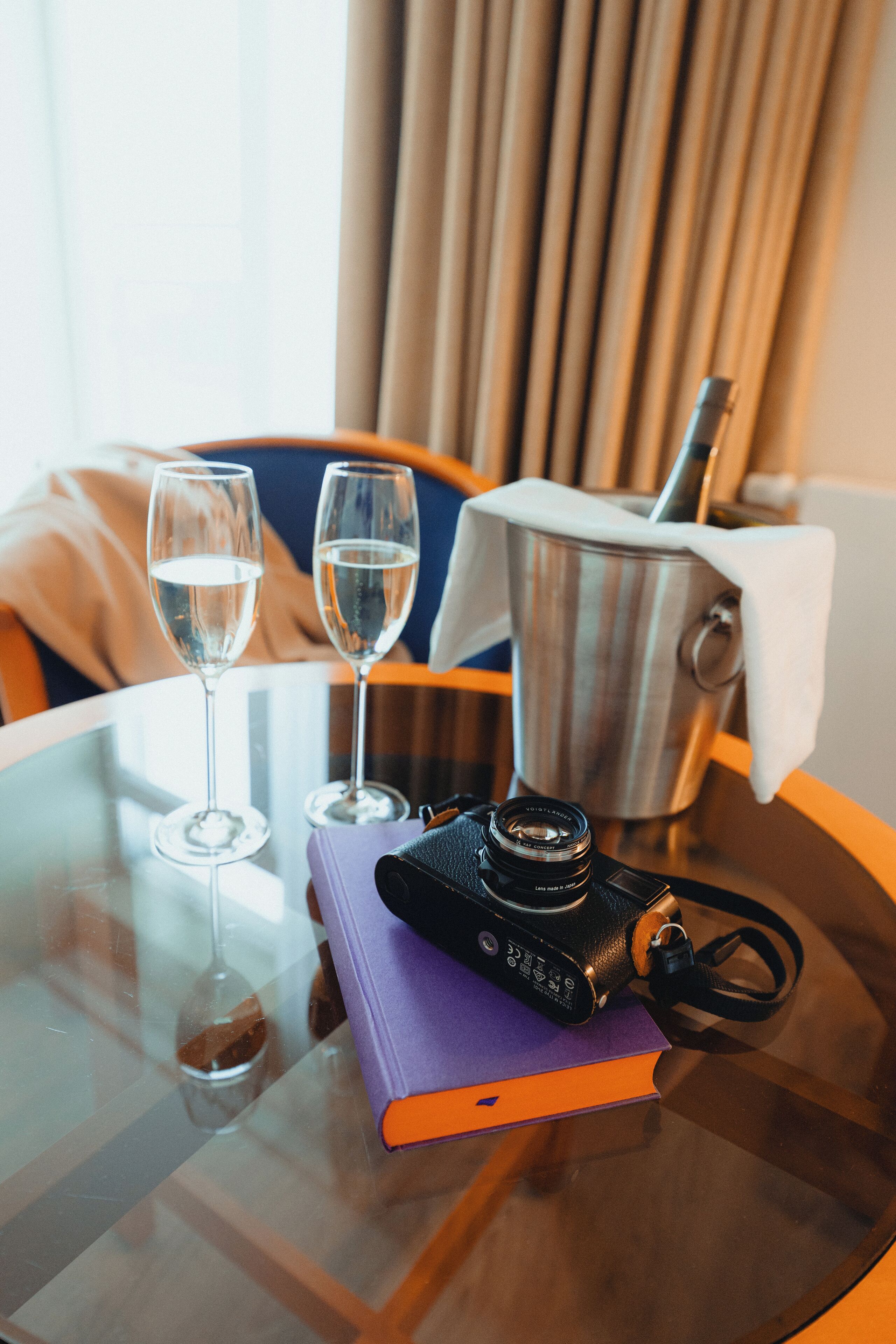 A glass table with two wine glasses, a camera, and a book.