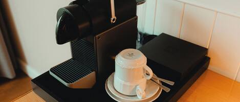A coffee maker on a tray, a cup, and a smartphone on a wooden table.
