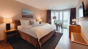 Habitación de hotel con una cama grande, dos mesitas de noche, un televisor, una silla y vistas al exterior.