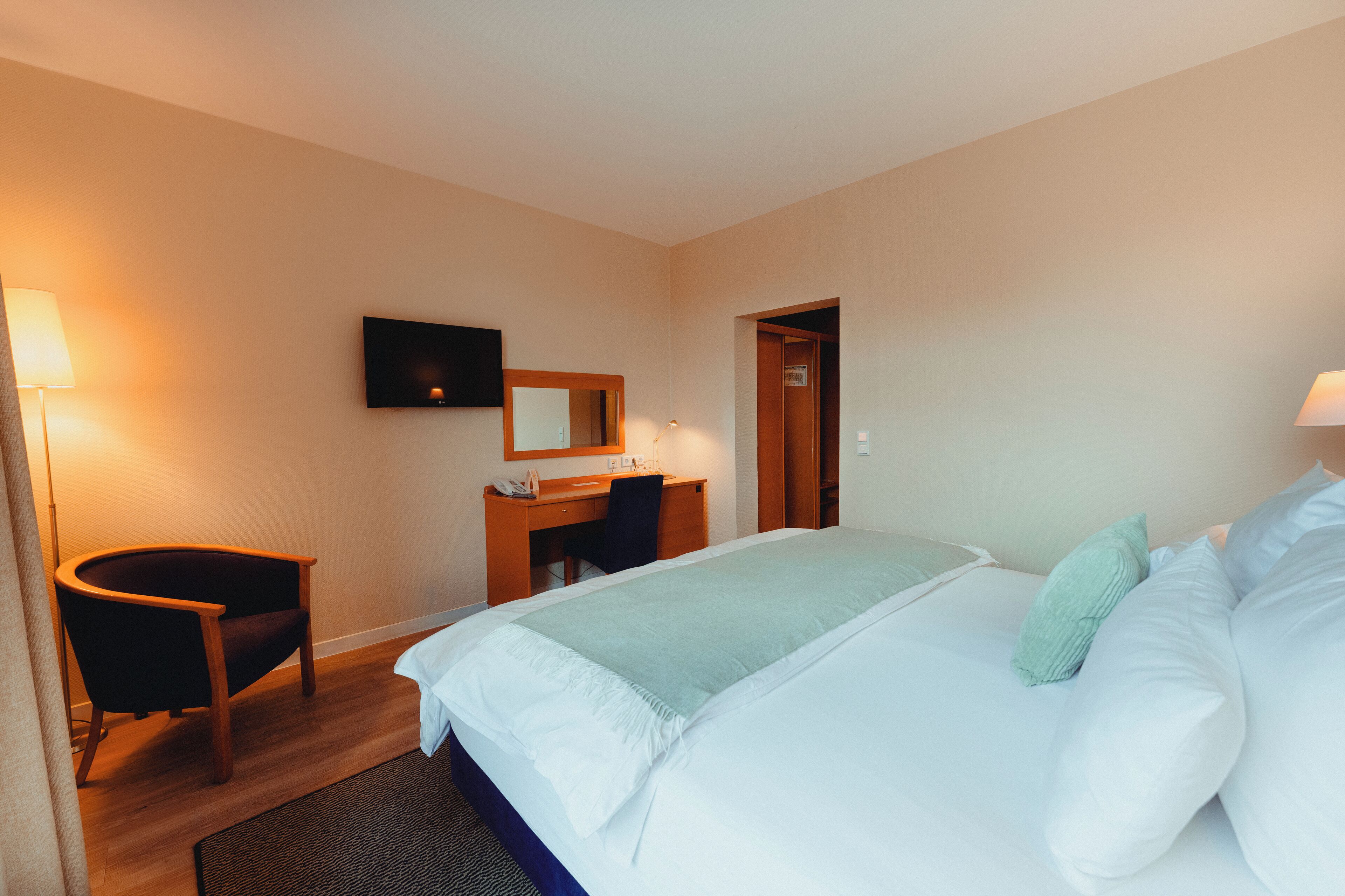 Una habitación de hotel con cama, escritorio, silla, televisor y puerta.