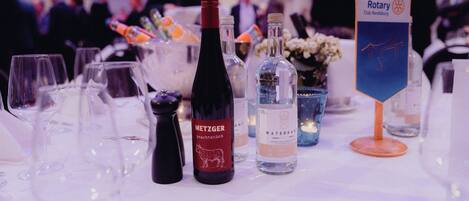 Mesa dispuesta con botellas de vino, copas y una botella de agua, con un cartel del Club Rotary al fondo.