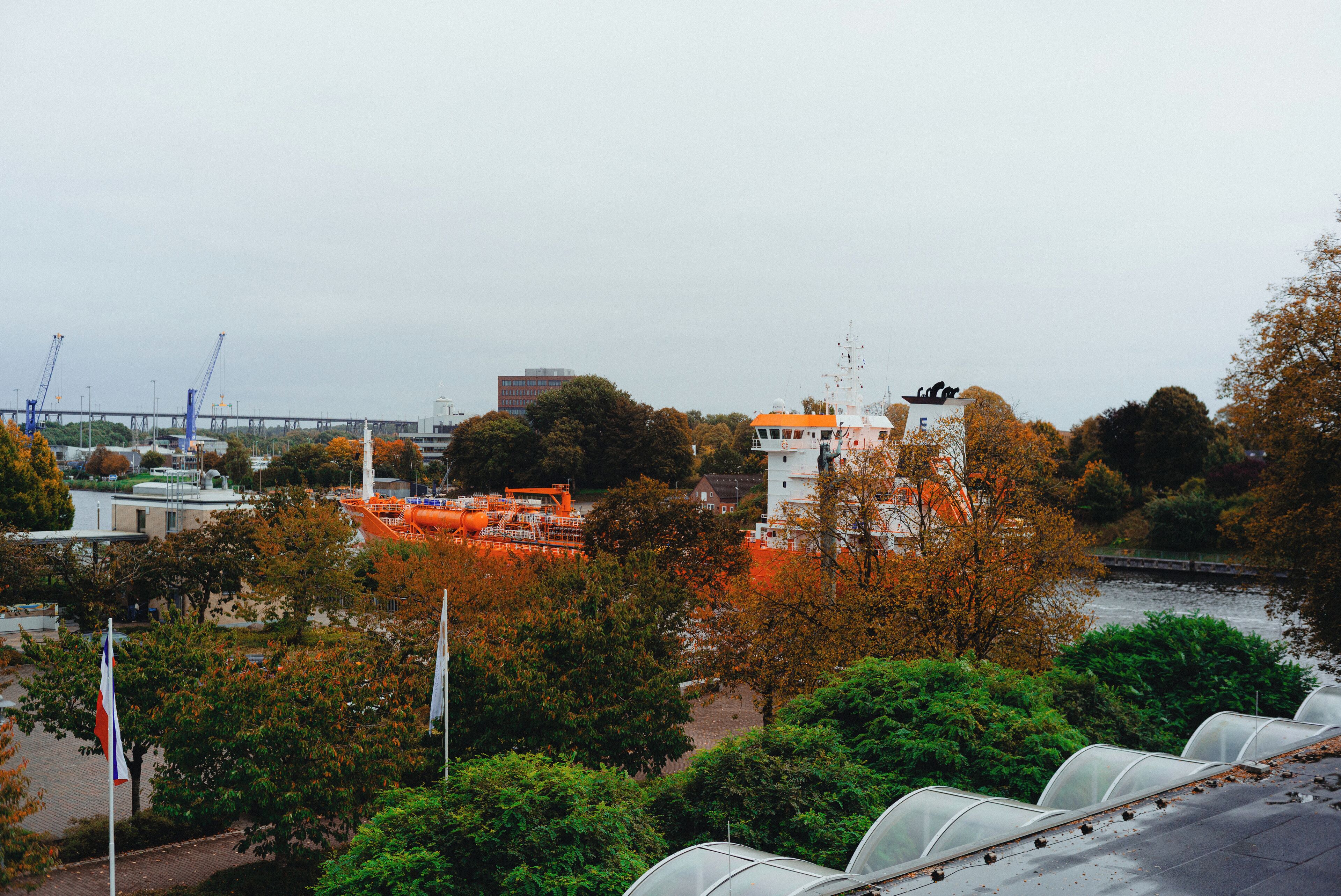 Blick auf einen Fluss mit einer Brücke, Bäumen und einem Gebäude mit weißer Fassade und orangenem Dach.