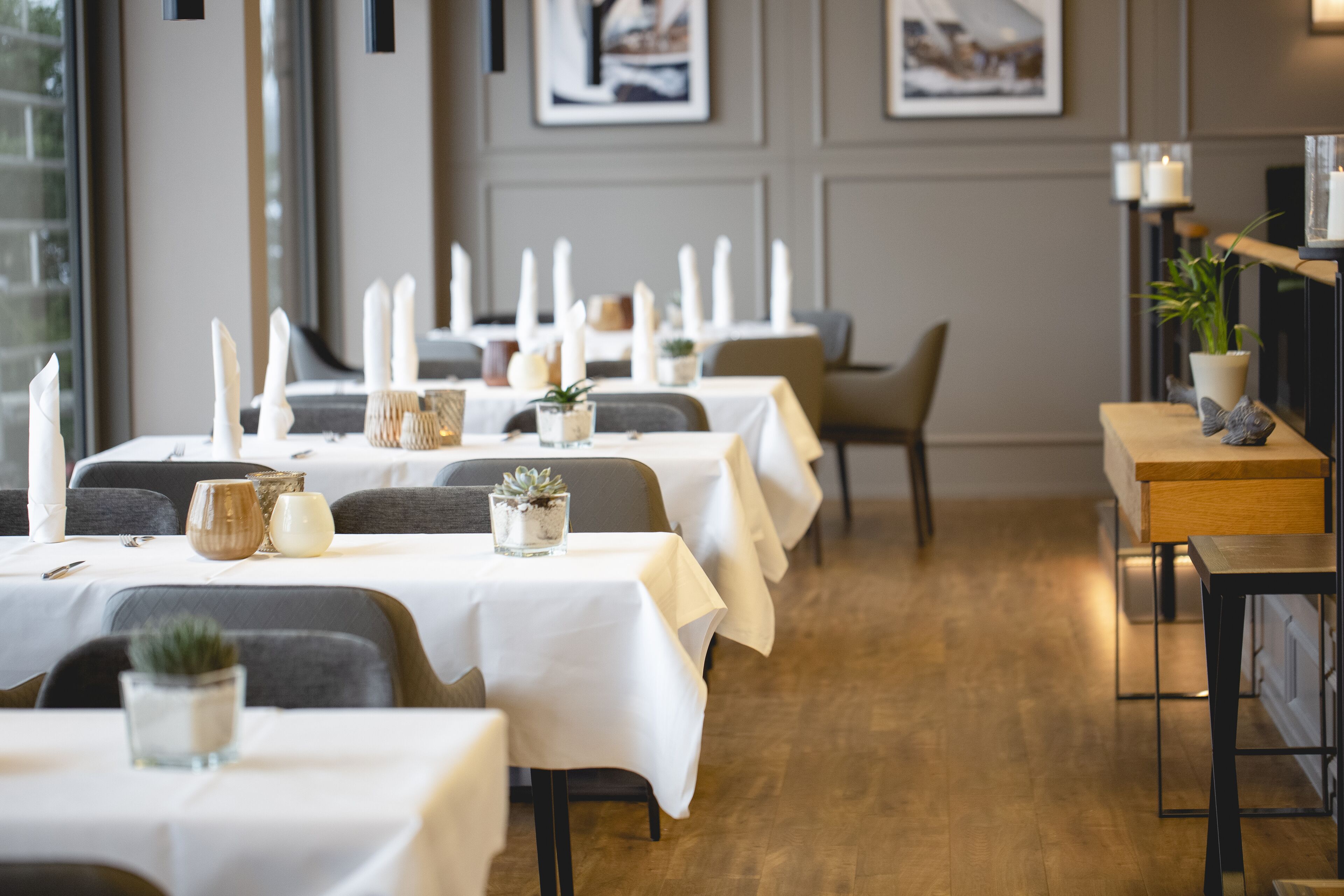 Un restaurant avec de nombreuses tables dressées pour le dîner, agrémentées de nappes blanches, de bougies et de petites plantes décoratives.