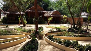 A garden with thatched-roof huts, surrounded by well-maintained flower beds and trees. - Mangroves & More (Sihanoukville)