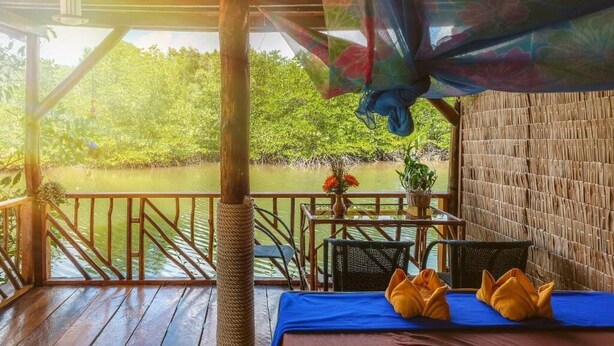 A wooden deck with a table and chairs, overlooking a calm body of water and lush greenery. - Mangroves & More (Sihanoukville)