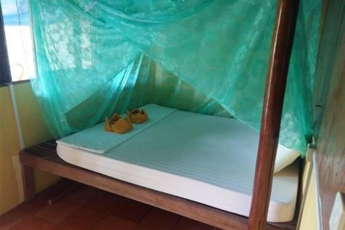 A single bed with a mosquito net and two slippers on it.