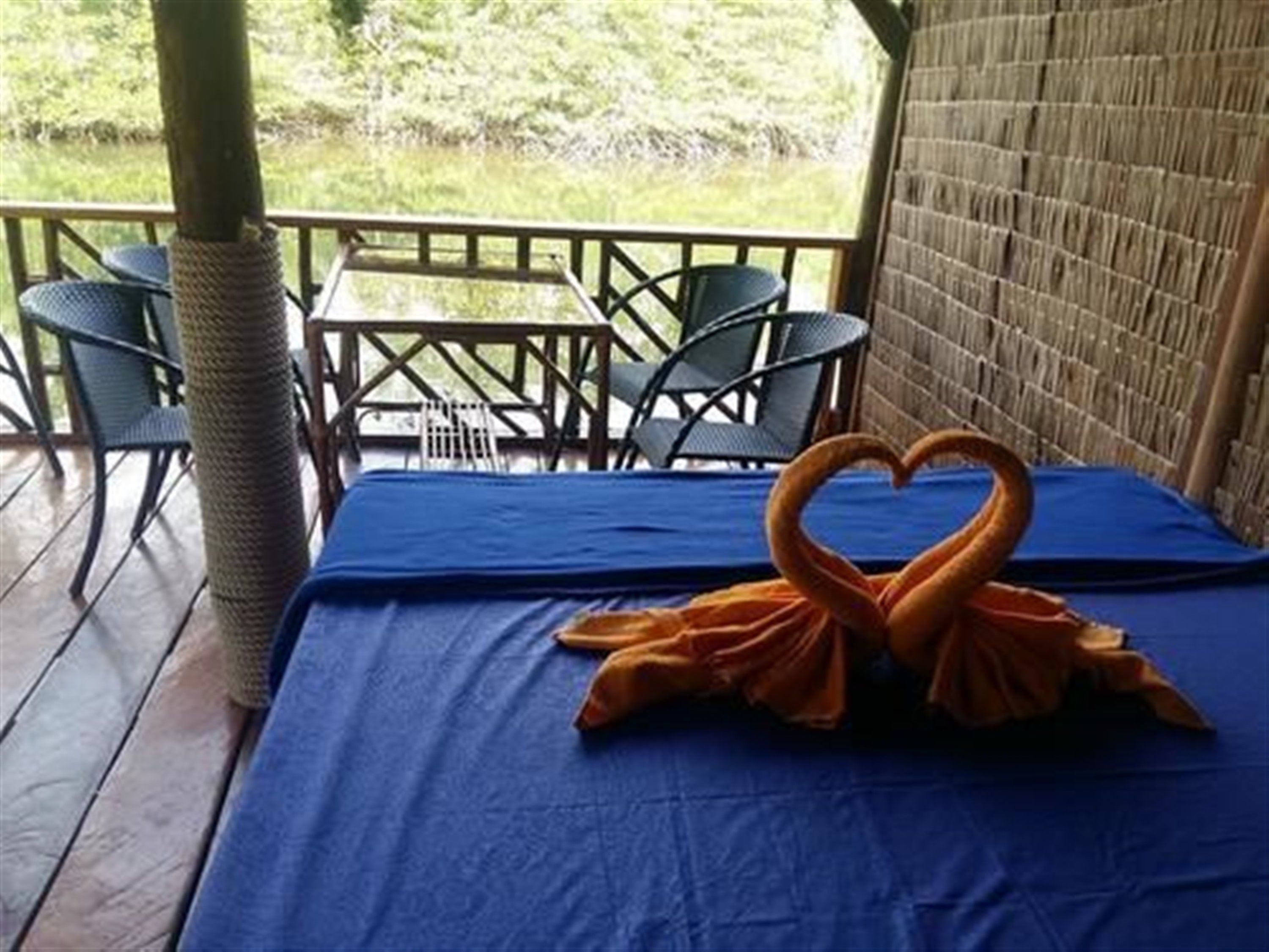 A room with a blue tablecloth, two swan-shaped towels, and a view of greenery outside.
