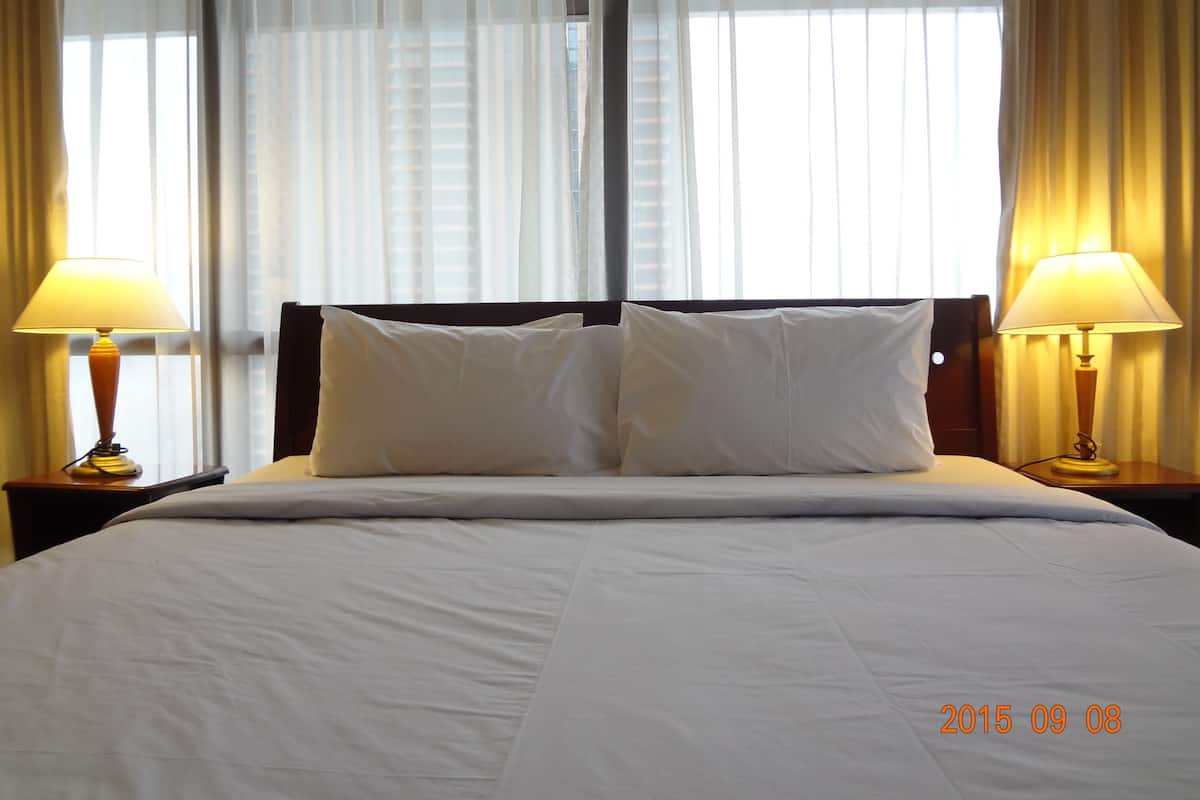 Habitación de hotel con una cama grande, dos lámparas de noche y cortinas traslúcidas.