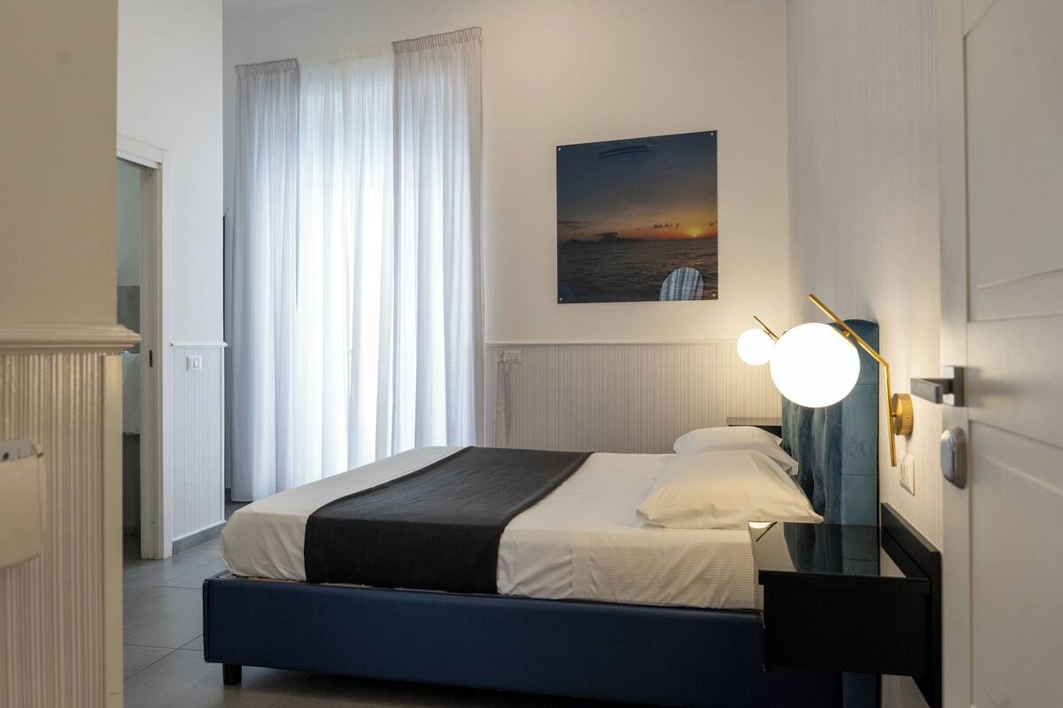 A neatly arranged hotel room with a bed, a bedside table, a nightstand, and a wall-mounted lamp.