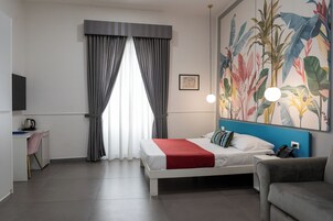 Habitación de hotel con cama, escritorio, silla, sofá, un cuadro y una ventana con cortinas.