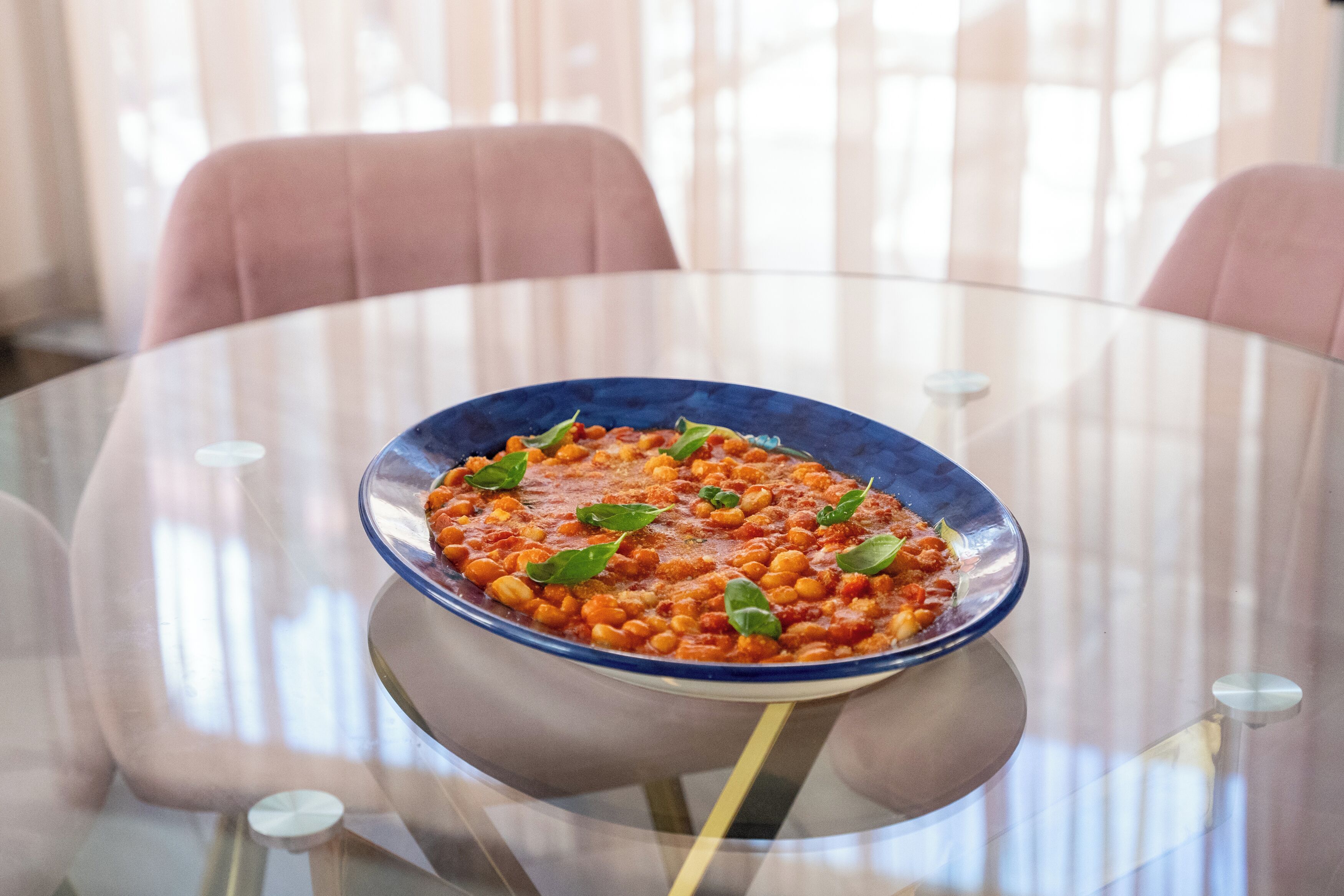 Une table en verre sur laquelle repose un saladier bleu contenant un plat de haricots, le tout entouré de chaises.