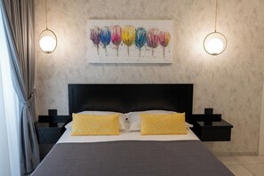 Ein Bett mit dunklem Kopfteil, zwei Nachttische mit Lampen und ein Gemälde bunter Blumen darüber.