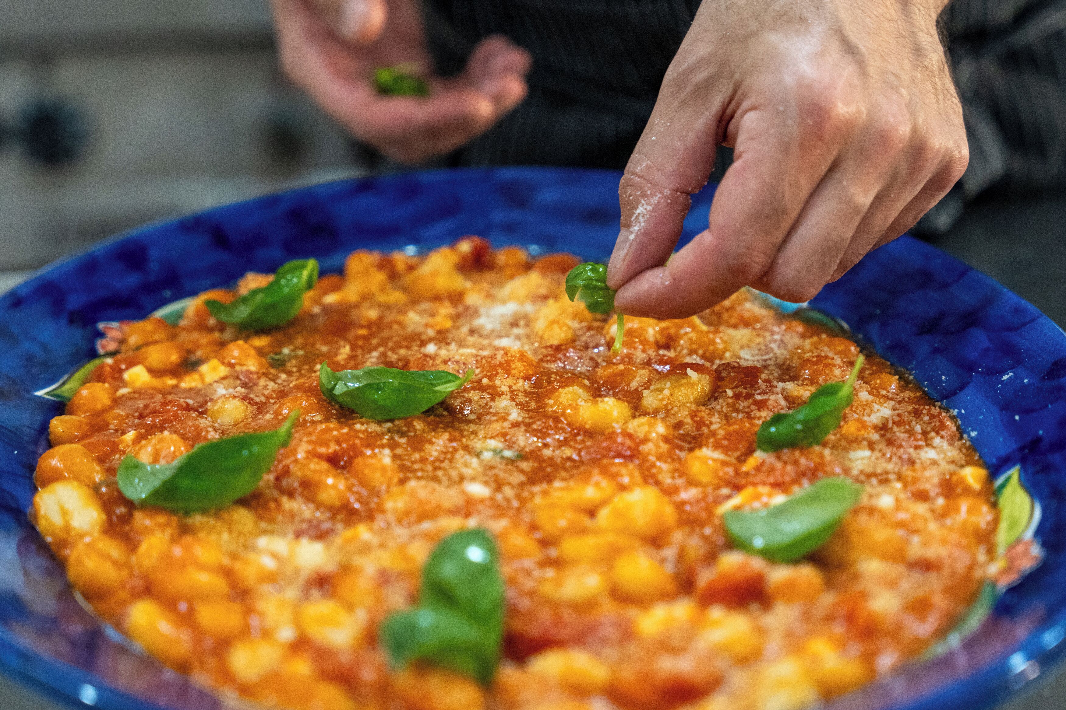 Primer plano de un plato con garbanzos, tomates y albahaca sobre un plato azul.