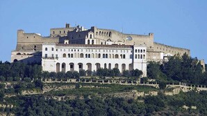 A large, historic building with multiple levels and arched windows, surrounded by greenery and a clear sky. - Hotel San Michele (Naples)