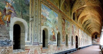 Un largo pasillo con frescos decorativos y techos abovedados.