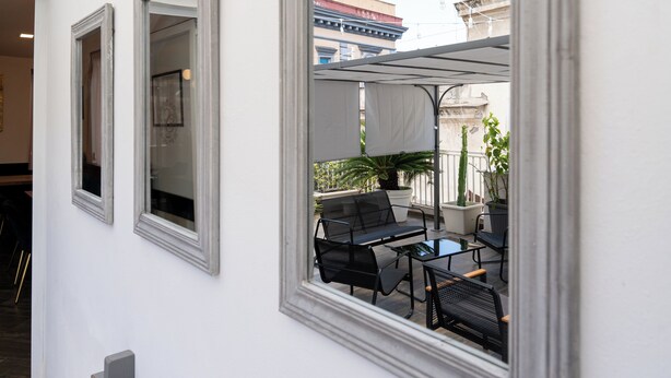A modern outdoor seating area with a table and chairs, a potted plant, and a view of the cityscape through a window. - Hotel San Michele (Naples)