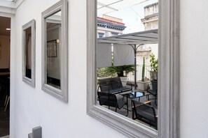 Un espacio moderno al aire libre con una mesa, sillas, una planta en maceta y vistas de la ciudad a través de un ventanal.