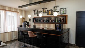 A bar area with a long counter, multiple stools, and a selection of bottles and glasses. - Hotel San Michele (Naples)