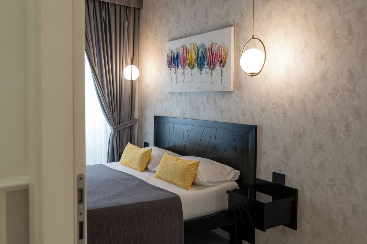 A modern bedroom with a bed, two bedside tables, a wall-mounted light, and a painting.