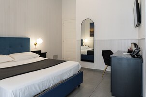 Ein modernes Hotelzimmer mit einem großen Bett, einem Schreibtisch, einem Sessel, einem Spiegel und einem an der Wand befestigten Fernseher.