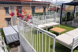 Een terras op het dak met witte reling, een kleine tafel en twee comfortabele stoelen.
