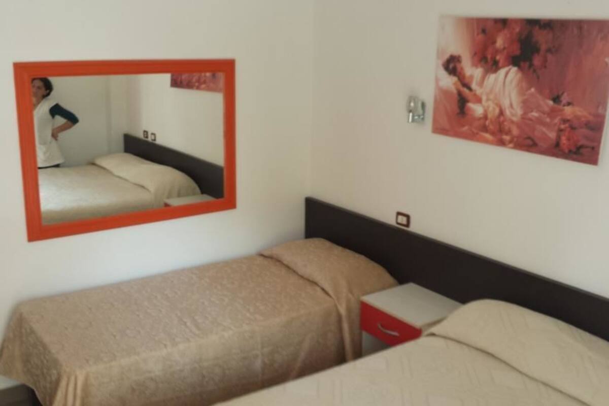 A hotel room with a single bed, a nightstand, a mirror, and a painting on the wall.