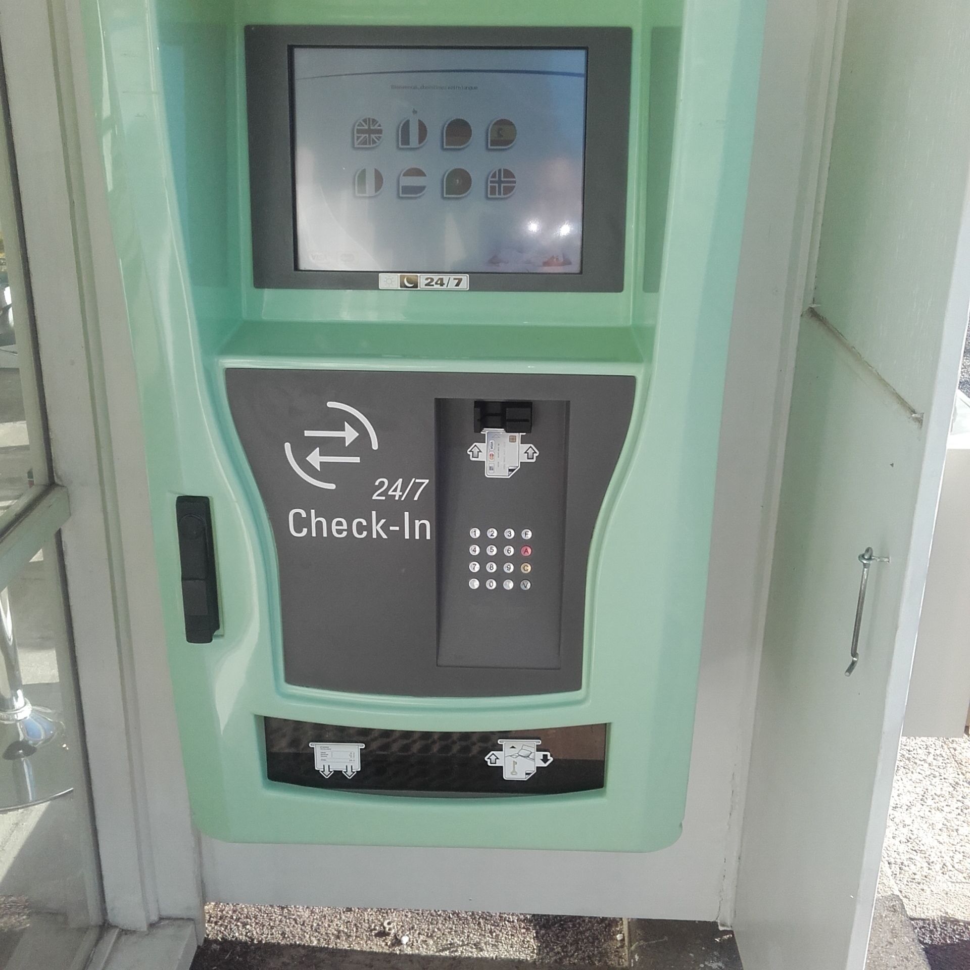 A 24/7 check-in kiosk with a keypad and a screen displaying various icons.