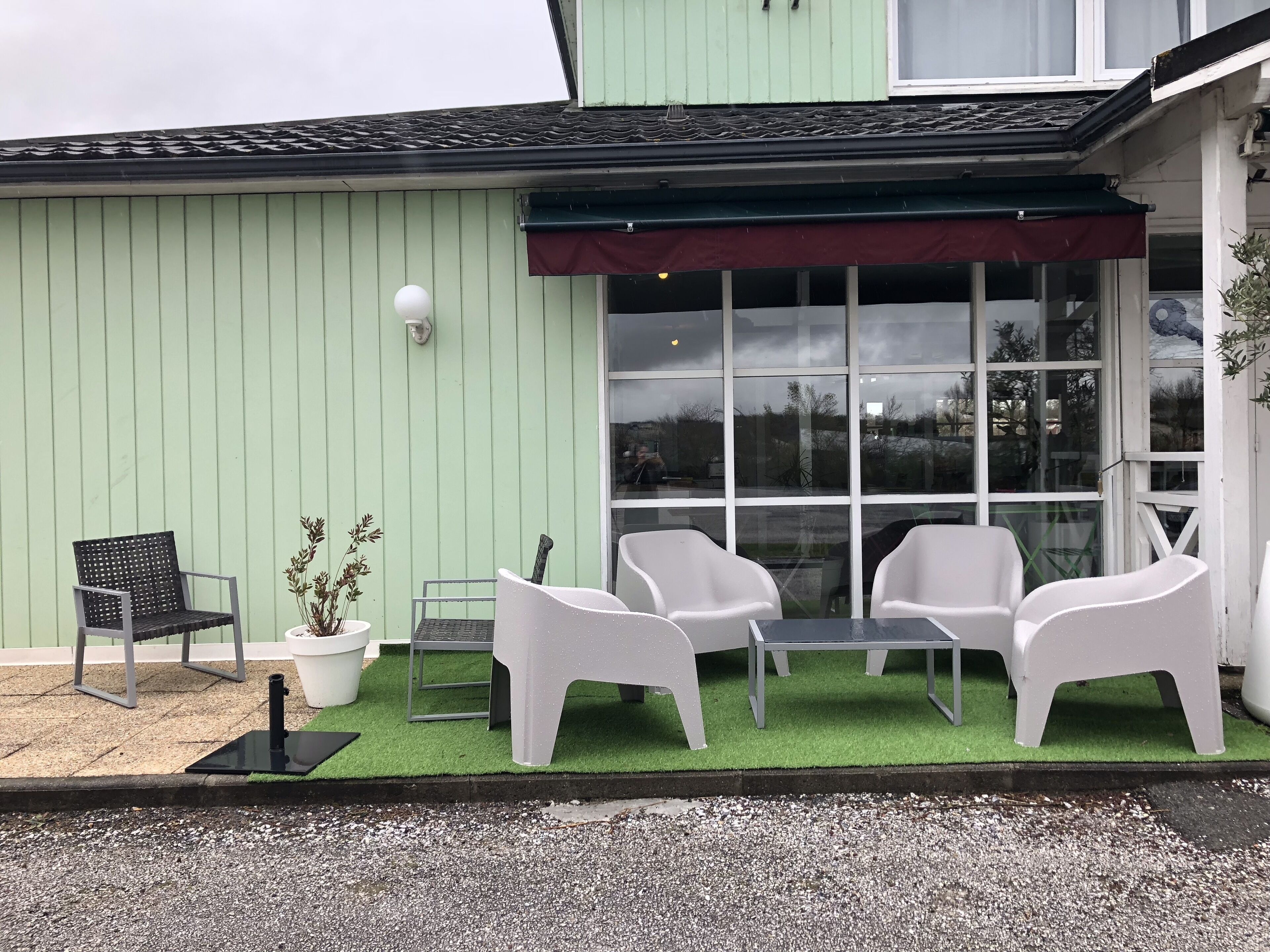 Une terrasse avec des sièges d’extérieur, un pot de fleurs et une fenêtre donnant sur les environs.
