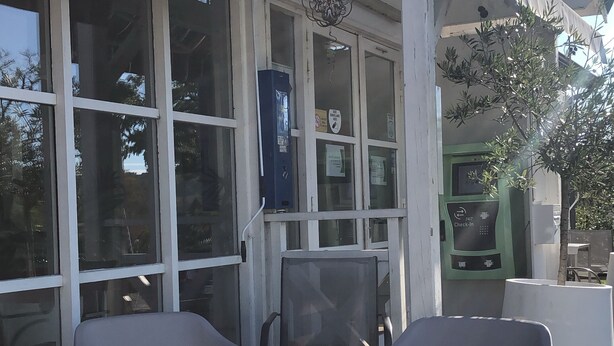 An outdoor seating area with two chairs and a table, a check-in kiosk, and a building with large windows and a green awning. - Le 81 Hôtel (Castres)