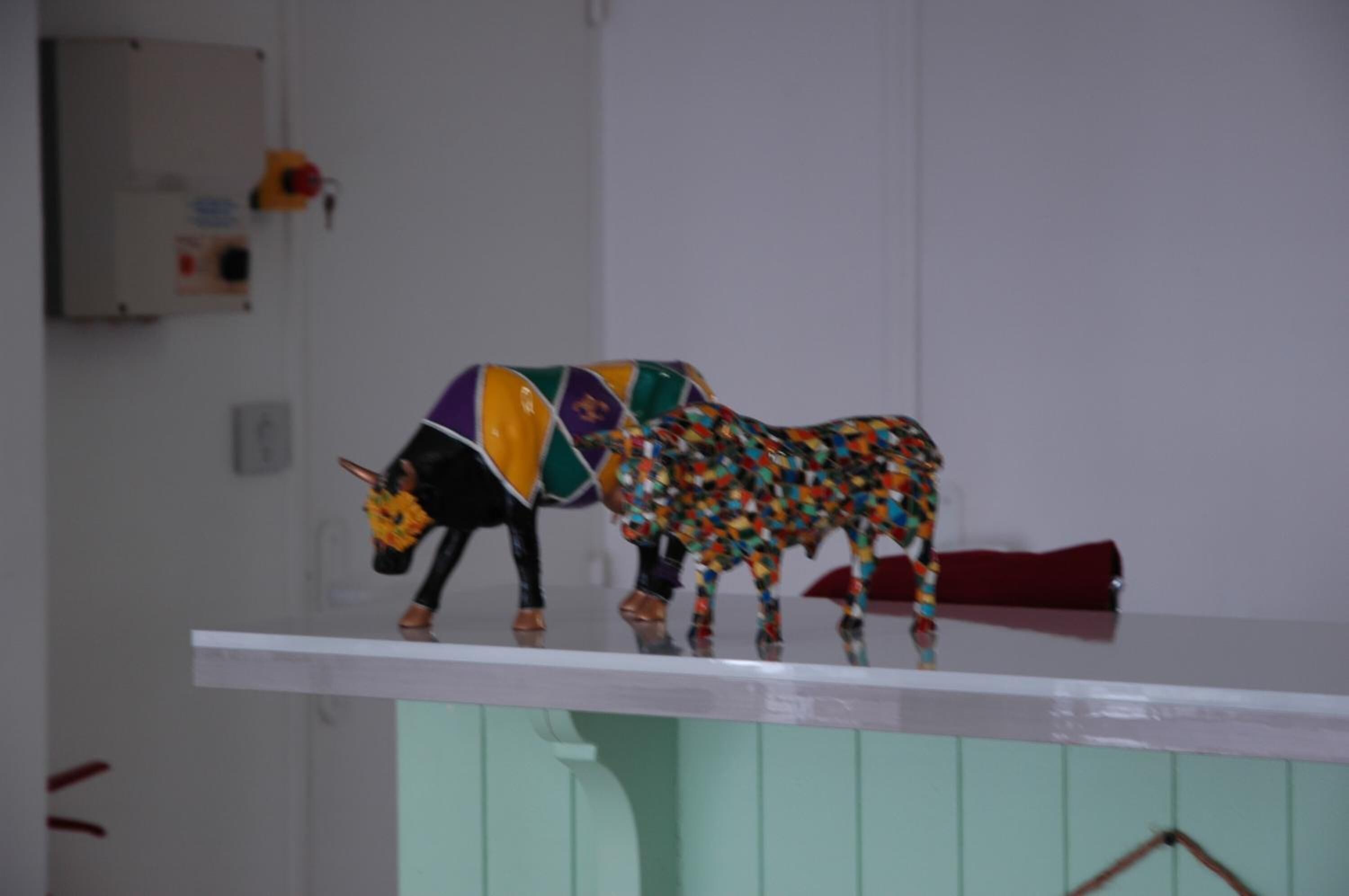 A colorful bull sculpture on a white shelf against a light green wall.