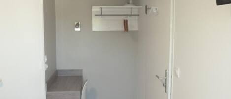 Een kleine, praktische kamer met een bureau, stoel en een ventilator aan de muur.