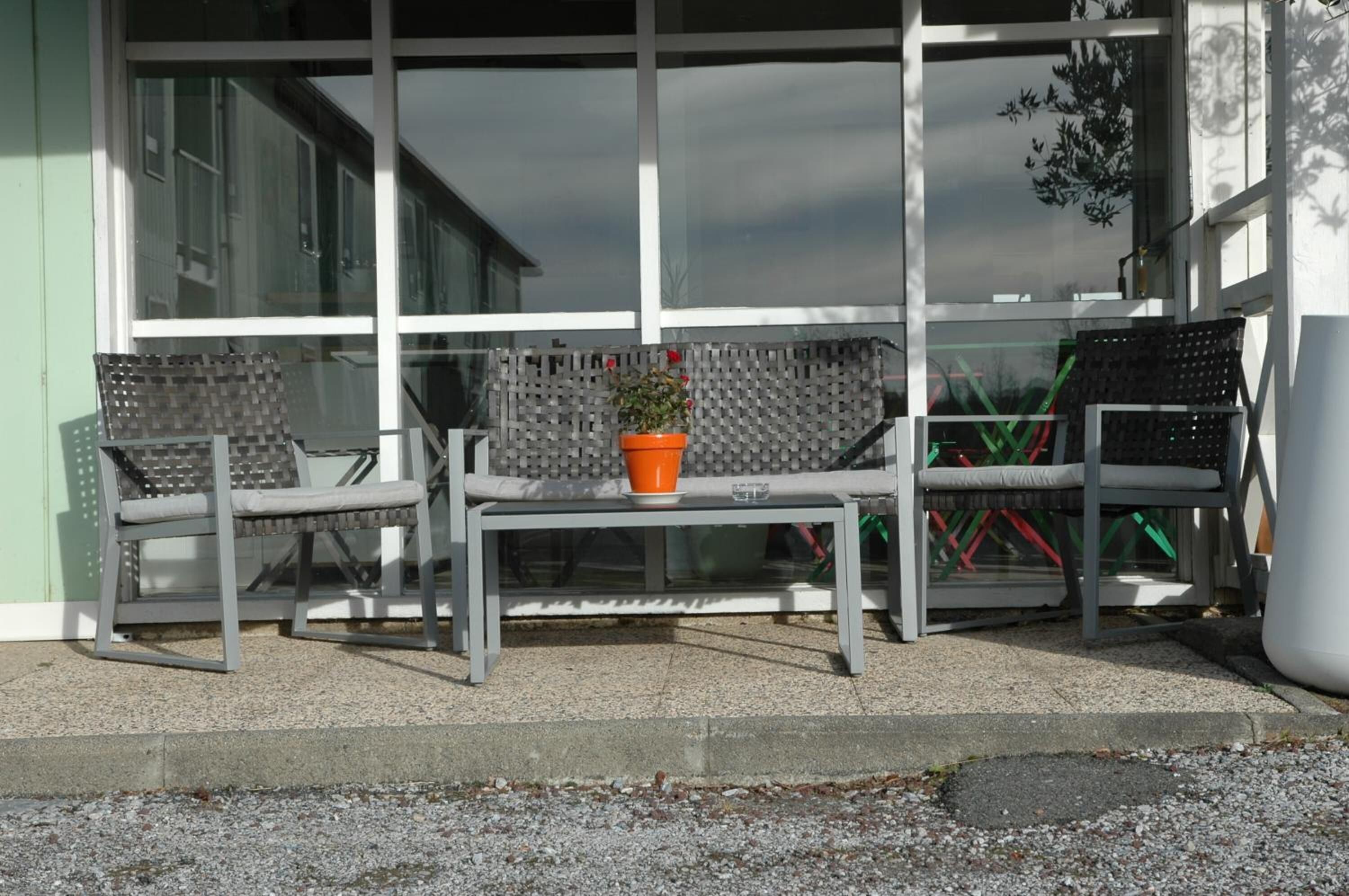 Un espacio al aire libre con dos sillas, una mesa, una planta en maceta y un panel de vidrio.