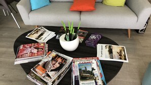 A living room with a grey sofa, three cushions, a black coffee table with magazines and a plant. - Le 81 Hôtel (Castres)