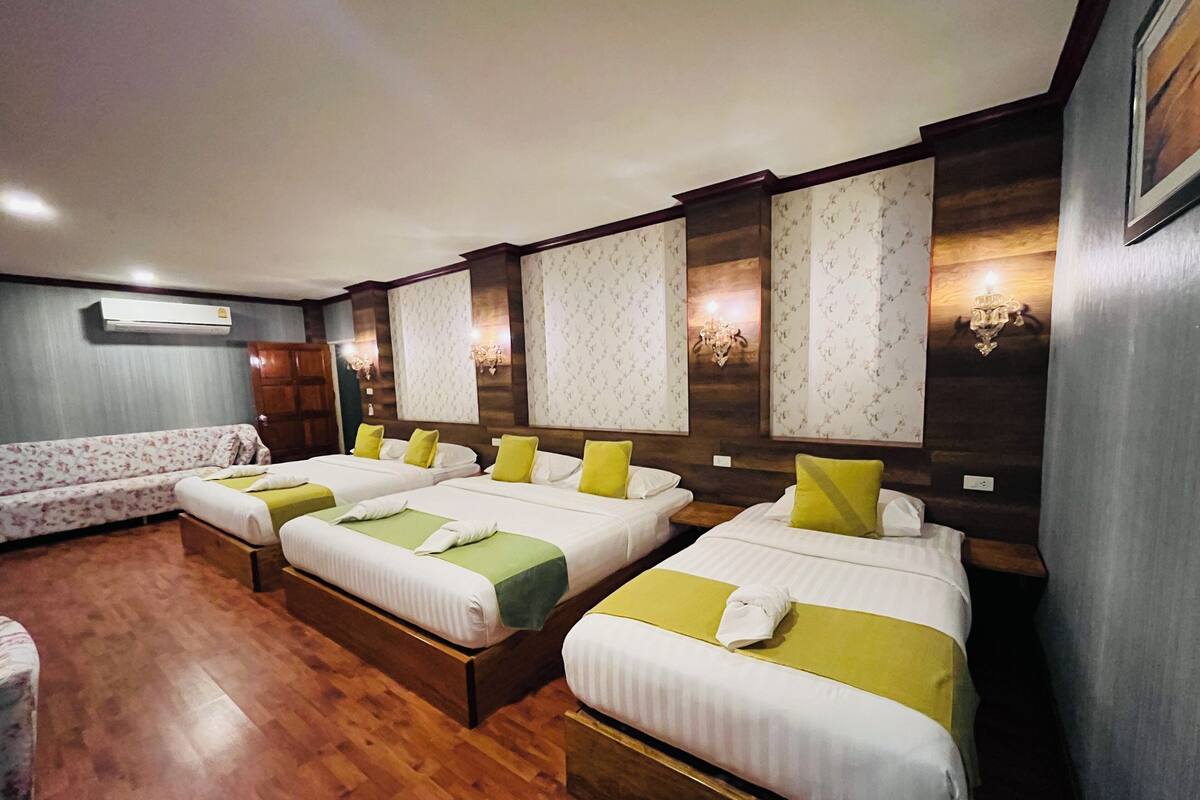 Habitación de hotel con cuatro camas individuales, un sofá, suelo de madera y un candelabro.