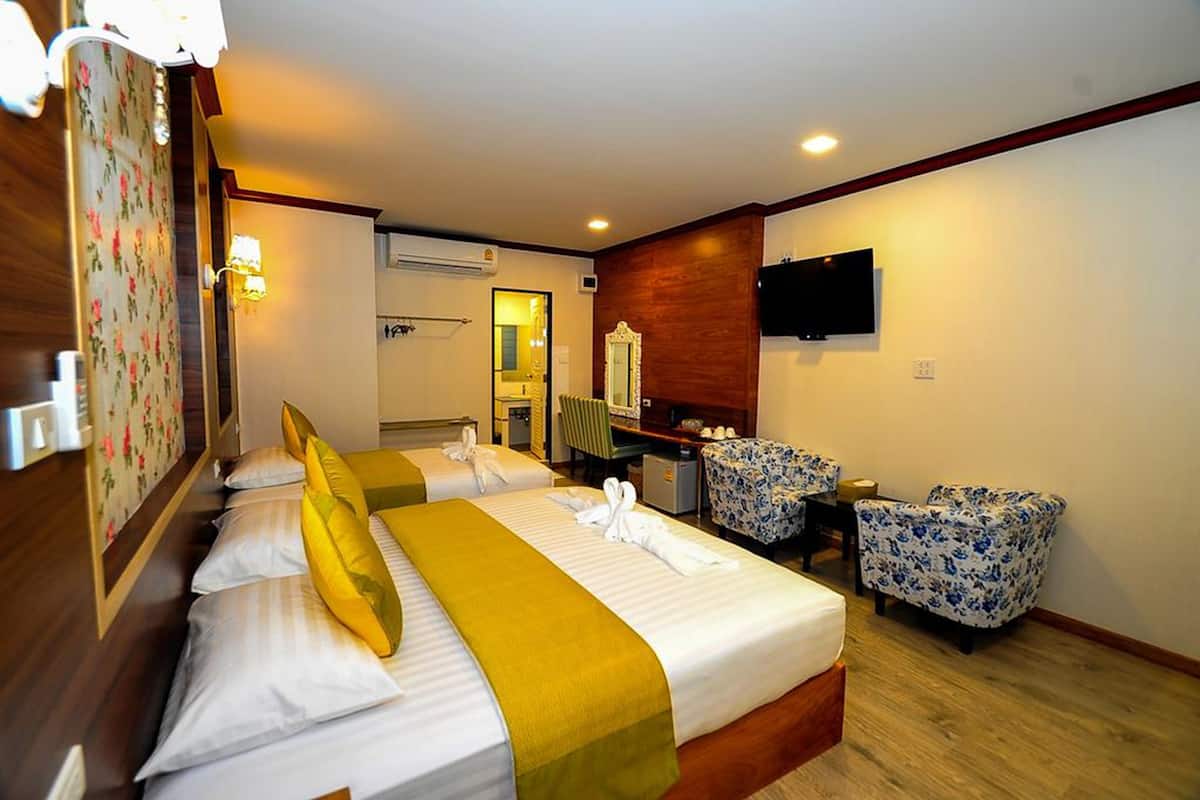 Una habitación de hotel con una cama, dos sillas, un escritorio, un televisor y un espejo.