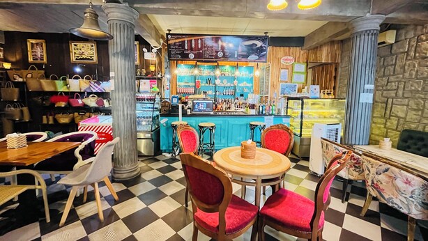 A bar area with a checkered floor, wooden chairs, a bar counter, and shelves with bottles. - Lenoi Buri (Khuan Khanun)
