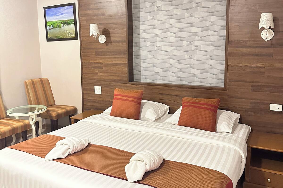 Habitación de hotel con una cama grande, una mesita, dos sillas, una lámpara de pared y un cuadro enmarcado.