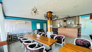 A restaurant with wooden tables and purple upholstered chairs, a reception desk, and a ceiling with a geometric pattern. - Lenoi Buri (Khuan Khanun)